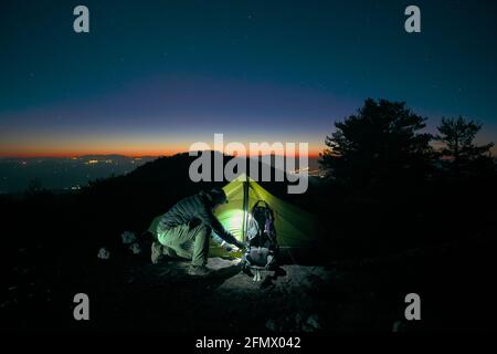 Outdoor-Abenteuer-Tourismus in der sizilianischen Natur ist ein Mann Betreten eines beleuchteten Zeltes bei Sonnenuntergang in den Bergen von Etna Park Stockfoto