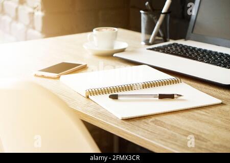 Laptop-Computer, Clipboard, Kaktus Heimpflanze, Verbrauchsmaterialien und gefaltete Gläser auf Holzschreibtisch in geräumigen Büro voller Sonnenlicht. Kreative Ideen des Designers Stockfoto