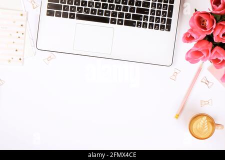 Feminine Nahaufnahme des Desktops, Laptop-Computertastatur, Tasse Kaffee mit Latte-Kunst, rosa Blumen. Minimal beschnittene flache Laienzusammensetzung, Notizbuch, Cappuccino Stockfoto