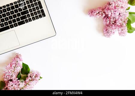 Zugeschnittenes Bild von Laptop-Tastatur und lila Blumen in minimaler Anordnung auf weißem Tischhintergrund. Feminine, flache Lay-Komposition mit pc-Notebook Stockfoto