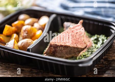 Köstliches rotes Fleisch Sous Vide Steak verpackt in tragbaren Take Entfernt Plastikbox und serviert mit knusprig gerösteten Kartoffeln und Herzhafte Spinat Dip und frisch Stockfoto