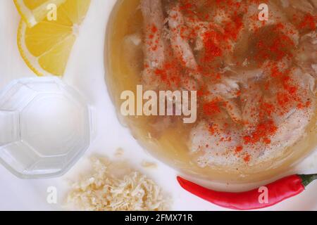 Ungarisches Schweinefleisch in Gelee, Kocsonya, mit roter Chili, Zitrone, geriebenem Meerrettich, Paprika, begleitet von einem Glas Palinka (ungarischer Obstbrand). Stockfoto