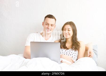 Paar im Bett mit Laptop. Junge amerikanische Männer und Frauen, Ehemann und Ehefrau, die sich verliebt haben, einen starrenden pc-Notebook-Computer zu halten. Männliche und weibliche Modell Surfen Surfi Stockfoto