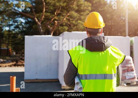 Der Architekt des Projekts steht auf der Baustelle eines Hauses, auf dem das Fundament gelegt und die Blöcke geliefert wurden. Bauarbeiter in einem Protective Stockfoto