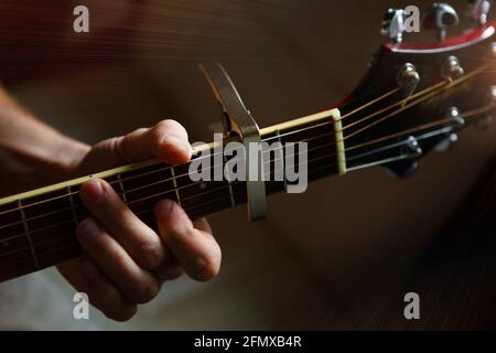 Die Hand eines Mannes auf dem Griffbrett einer Gitarre läuft mit den Fingern durch die Saiten und spannt die Akkorde. Instrumentalmusik, Gitarrenunterricht auf Noten Stockfoto