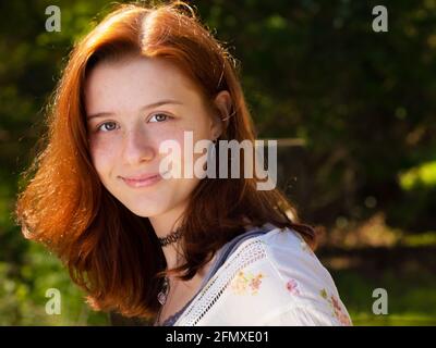 Hübsches rothaariges High School- oder College-Mädchen mit blaugrünen Augen, das im Sommer in legerer Kleidung in Wäldern posiert Stockfoto