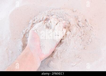 Die Hand des Typen nimmt oder berührt den weißen Strandsand aus nächster Nähe. Stockfoto