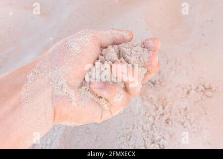 Die Hand des Typen nimmt oder berührt den weißen Strandsand aus nächster Nähe. Stockfoto