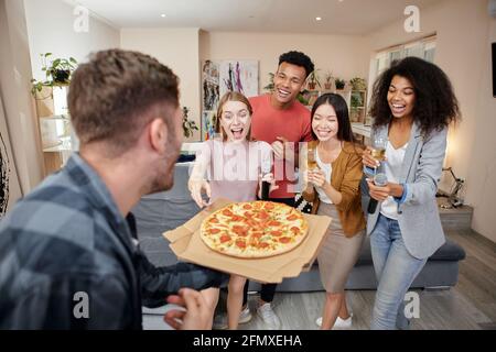 Für Ihre Party. Aufgeregte multikulturelle Freunde bestellten Pizza, während sie eine Karaoke-Party hatten und mit einem Mikrofon in der modernen Wohnung sangen Stockfoto