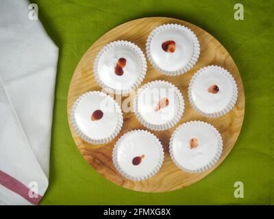 Mehrere rohe französische Dessert-Meringues mit Erdbeersauce, verziert mit einer Serviette auf einer grünen Tischdecke und einem runden Holzteller. Draufsicht Stockfoto