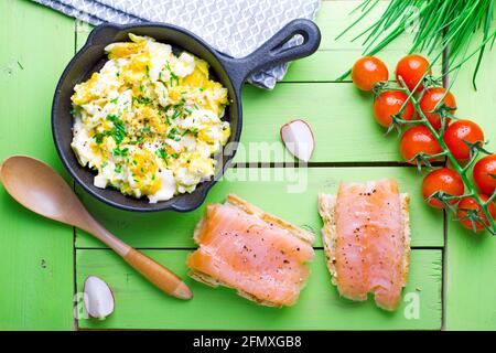 Rührei in einer Pfanne, Toast mit geräuchertem Lachs, Tomaten, auf einem alten grünen Holztisch Stockfoto