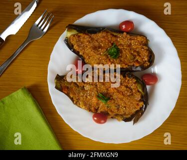 Gefüllte Auberginen, Auberginen mit Bolognese-Sauce und frische Kirschtomaten in einer weißen Schale, die mit Besteck und grüner Serviette dekoriert ist. Draufsicht Stockfoto