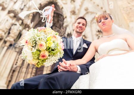 Bräutigam holding Blumenstrauß Kugel sitzend mit Braut außerhalb der Kirche Stockfoto