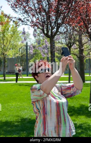 Krasnodar, Russland - 2 2021. Mai: Wanderfrau fotografiert mit Handykamera im Park mit blühenden Bäumen Stockfoto