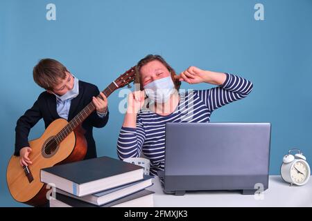 Der Sohn mit der Gitarre hindert seine Mutter daran, aus der Ferne am Computer aus der Ferne zu arbeiten. Probleme bei der Remote-Arbeit während einer Sperre Stockfoto