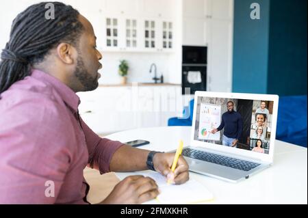 Fokussierter afroamerikanischer Student mit Locks-Frisur mit Laptop-Computer zum Studieren in der Ferne, Schwarzer schaut sich Online-Kurse an, macht Notizen, beteiligt Webinar Stockfoto