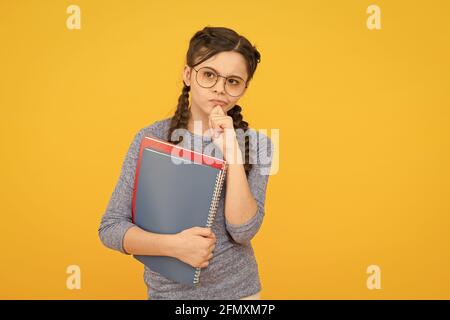 Nachdenkliches Schulmädchen. Mädchen kleine Schülerin. Schüler mit Zöpfen, der zur Schule geht. Schulmädchen Alltag. Buch aus der Bibliothek nehmen. Kurse für Begabte Stockfoto