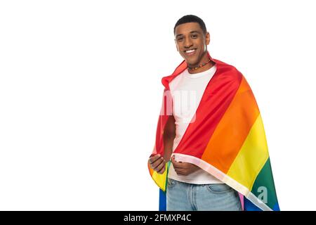 Junger afroamerikanischer Mann, eingewickelt in lgbt-Flagge, lächelnd auf weiß isolierte Kamera Stockfoto