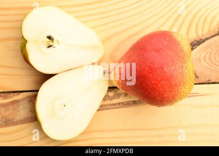 Eine ganze und zwei Hälften reifer Bio-Birnen, Nahaufnahme, auf einem Holztisch, Draufsicht. Stockfoto