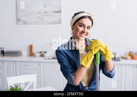 Hausfrau in Gummihandschuhen mit Wischmopp und lächelnd vor der Kamera Stockfoto