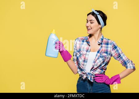 Lächelnde Hausfrau hält Flasche Waschmittel isoliert auf gelb Stockfoto