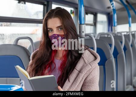 Eine Frau sitzt in einem Bus mit einem Buch, aber Blick auf die Kamera Stockfoto