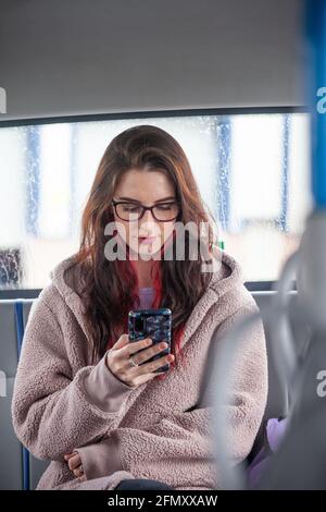 Porträt einer jungen Frau, die mit dem Bus unterwegs ist und Zelle anschaut Telefon Stockfoto