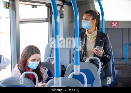 Zwei Frauen in ihren zwanzig Jahren, die in einem Bus unterwegs sind Gesichtsmasken Stockfoto