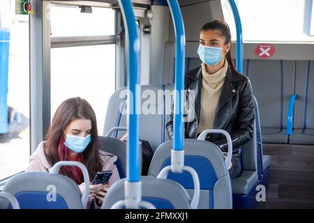 Zwei Frauen in ihren zwanzig Jahren, die in einem Bus unterwegs sind Gesichtsmasken Stockfoto