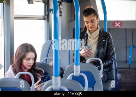 Zwei Frauen im Alter von 20 Jahren, die in einem Bus unterwegs sind und ihre Telefone angusten. Stockfoto