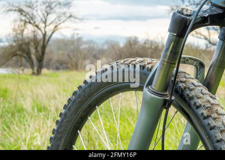 Teil des Vorderrads und der Gabel eines Mountainbikes auf einem verschwommenen Hintergrund aus grünem Gras und Wald und Himmel. Gesundes Lifestyle-Konzept Stockfoto