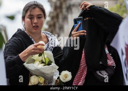 London, Großbritannien. Mai 2021. Eine Frau verteilt weiße Rosen, während Tausende von Menschen an einer Notkundgebung teilnehmen, die aus Solidarität mit dem palästinensischen Volk besteht, das vor der Downing Street von der palästinensischen Solidaritätskampagne, den Freunden von Al Aqsa, der Koalition „Stoppt den Krieg“ und dem palästinensischen Forum in Großbritannien organisiert wurde. Die Kundgebung fand aus Protest gegen israelische Luftangriffe auf Gaza, die Entsendung israelischer Truppen gegen Gläubige in der Al-Aqsa Moschee während des Ramadan und Versuche statt, palästinensische Familien aus dem Stadtteil Sheikh Jarrah in Ostjerusalem gewaltsam zu verdrängt. Kredit: Mark Kerrison/Alamy Live Nachrichten Stockfoto