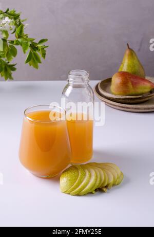 Saft mit Fruchtfleisch in einem Glas und einer Glasflasche. In der Nähe liegt die Hälfte der Birne auf einem hellen Hintergrund. Das Konzept der gesunden Ernährung, selektiver Fokus Stockfoto