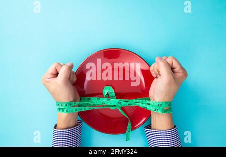 Gefesselte Hände eines Mannes mit einem Maßband und leerem Teller. Willenskraft zum Abnehmen. Stockfoto