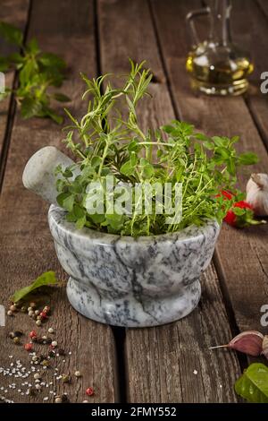 Duftende Kräuter in Mörtel auf Holztisch mit Gewürzen und Öl Stockfoto