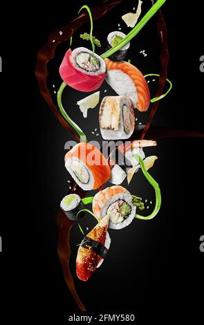 Verschiedene Sushi-Sorten mit in der Luft schwebenden Zierleisten auf schwarzem Hintergrund Stockfoto