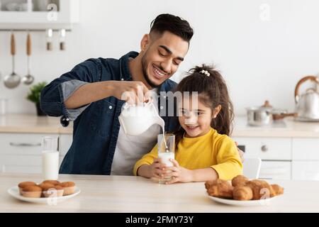 Glücklicher Arabischer Vater Und Tochter, Die Gebäck Essen Und Milch Trinken In Der Küche Stockfoto