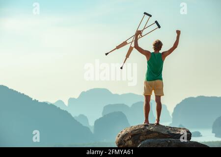 Der behinderte Mann steht in der Siegerpose auf einem großen Felsen und blickt auf Meer und Berge. Gesundheits- oder Versicherungskonzept Stockfoto