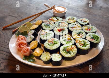 Großes Set mit Sushi und Brötchen. Große Rollensätze auf weißen Tellern auf einem Holzhintergrund. Perspektivische Ansicht Stockfoto