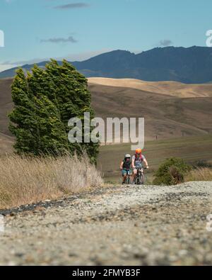 Zwei Radfahrer fahren auf dem Otago Rail Trail im starken Wind, Südinsel. Vertikales Format. Stockfoto
