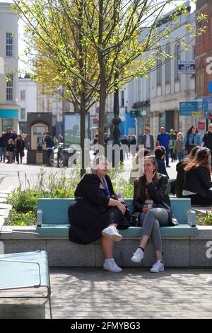 Cheltenham Gloucestershire Großbritannien 17. April 2021 zwei junge Frauen treffen sich und plaudern während der Mittagspause, sitzen im Stadtzentrum von Cheltenham Stockfoto
