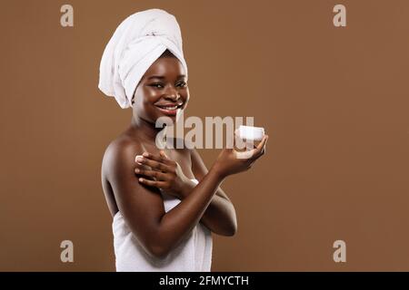 Self-Care-Konzept. Schöne Schwarze Dame Mit Handtuch Auf Dem Kopf Anwendung Feuchtigkeitsspendende Creme Stockfoto