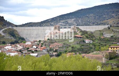 Enciso Stadt mit dem Damm oben. Häuser der Stadt, ihre Kirche und Burg, hinter der Betonmauer. Stockfoto