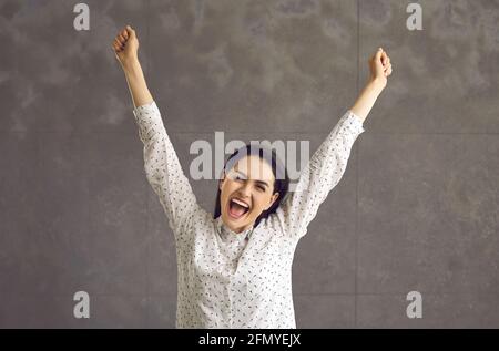 Junge optimistische Frau schreit und freut sich mit erhobener Hand Studio Aufnahme Stockfoto