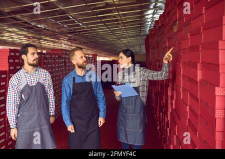 Der Lagerleiter der Schuhfabrik spricht mit den in der Nähe stehenden Arbeitern Reihen von Schuhkartons Stockfoto