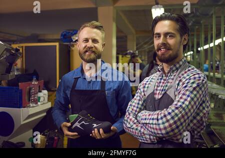 Portrait von glücklichen Arbeitern in der Schuhfabrik mit modernen Sneakers im Stehen In der Werkstatt Stockfoto