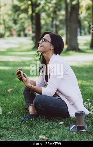 Geschäftsfrau sitzt im Sommer Gras Park mit Laptop. Arbeitet Remote während der Quarantäne. Weicher, selektiver Fokus. Stockfoto