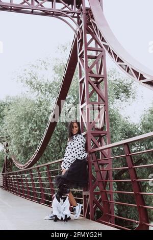 Eine schöne junge Frau in einem flauschigen Rock und einer gepunkteten Bluse auf der Brücke läuft mit ihrem Staffordshire Bull Terrier Hund. Weicher selektiver Fokus Stockfoto