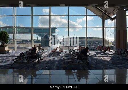 Ein paar Passagiere warten vor einem riesigen Fenster auf ihren Flug und bieten einen Blick auf Chek Lap Kok, den internationalen Flughafen von Hongkong. Stockfoto