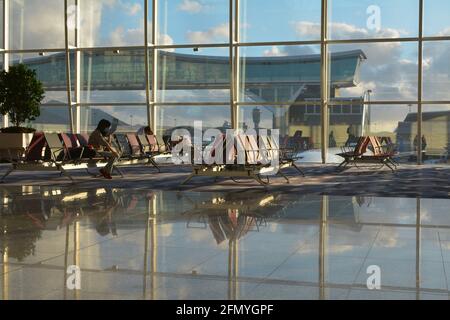 Ein paar Passagiere warten vor einem riesigen Fenster auf ihren Flug und bieten einen Blick auf Chek Lap Kok, den internationalen Flughafen von Hongkong. Stockfoto